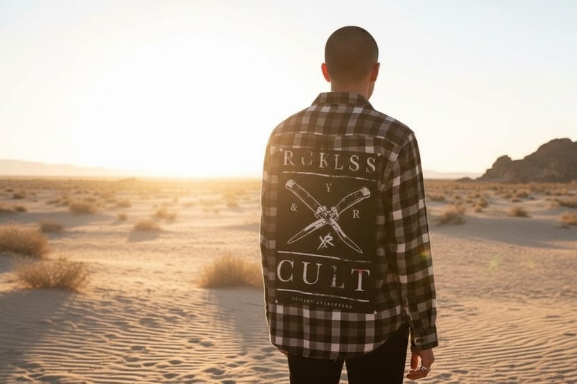 Person wearing a plaid shirt with graphic design, standing in a desert during sunset.